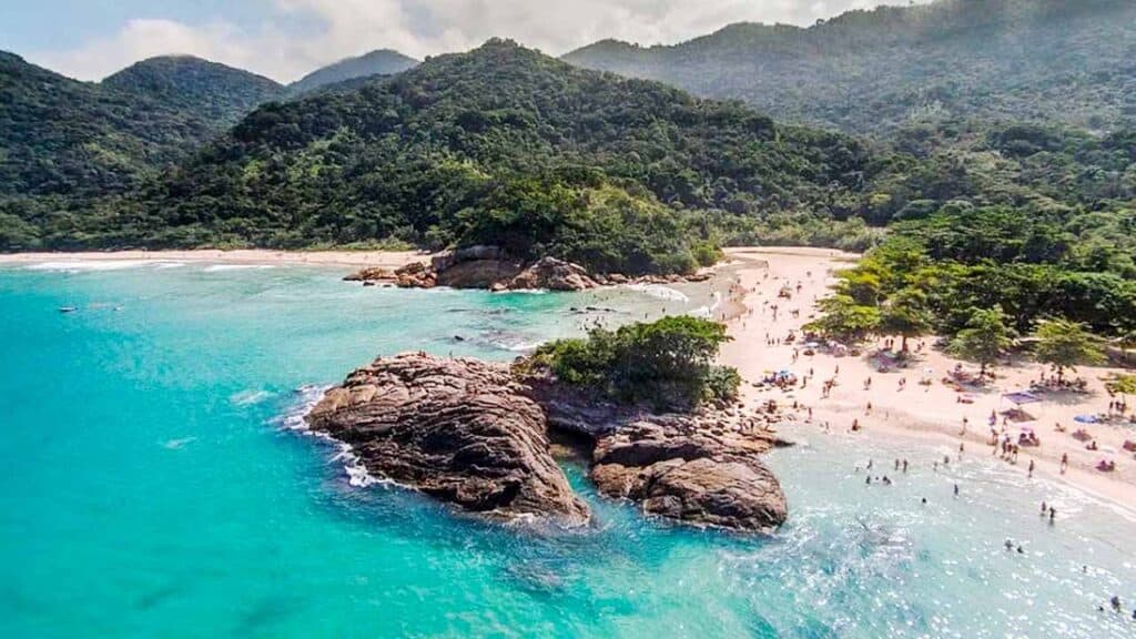 Beach with rocky formations and lush green mountains in the background.