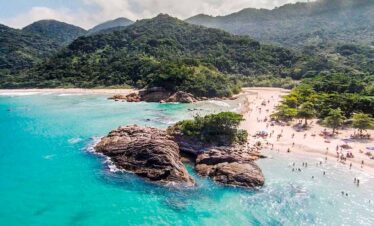 Beach with rocky formations and lush green mountains in the background.