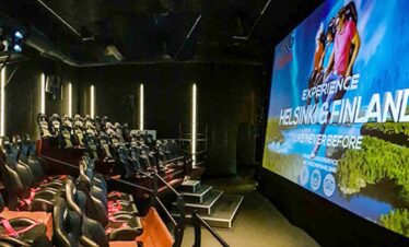 Modern cinema with seats and a large screen displaying Helsinki Finland scenery.