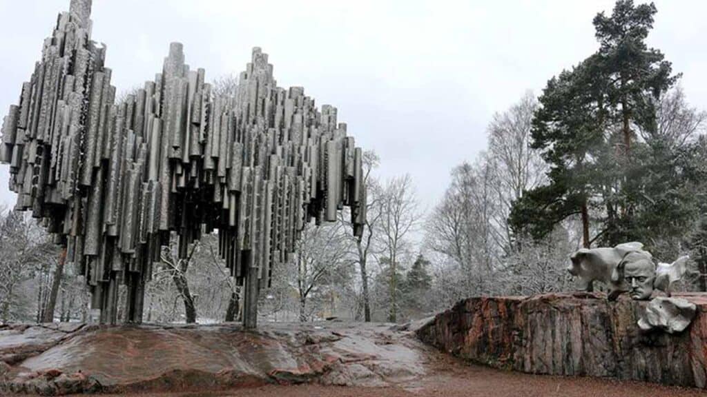Modern metallic sculpture of a boar in a park setting.