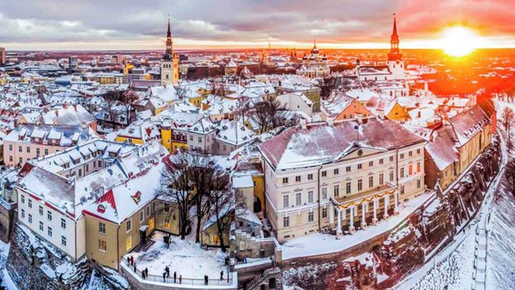 A panoramic view of a snow-covered historic city during sunset, showcasing colourful buildings and c.
