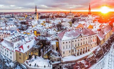 A panoramic view of a snow-covered historic city during sunset, showcasing colourful buildings and c.