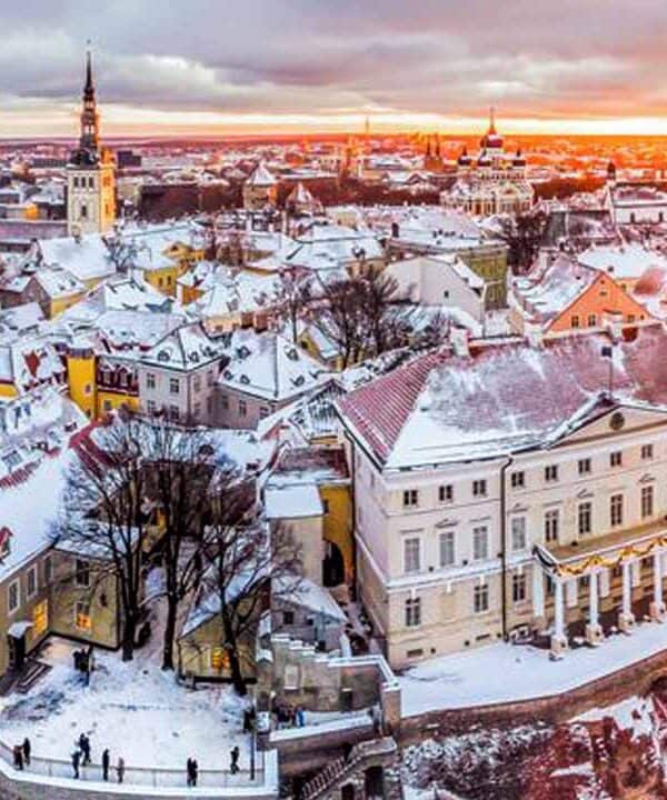 A panoramic view of a snow-covered historic city during sunset, showcasing colourful buildings and c.