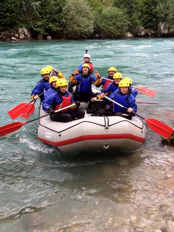 Group of people white water rafting on a river, wearing helmets and life jackets.