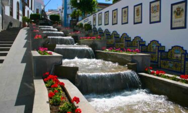 Water feature with cascading waterfalls and colourful flowers in a picturesque village setting.