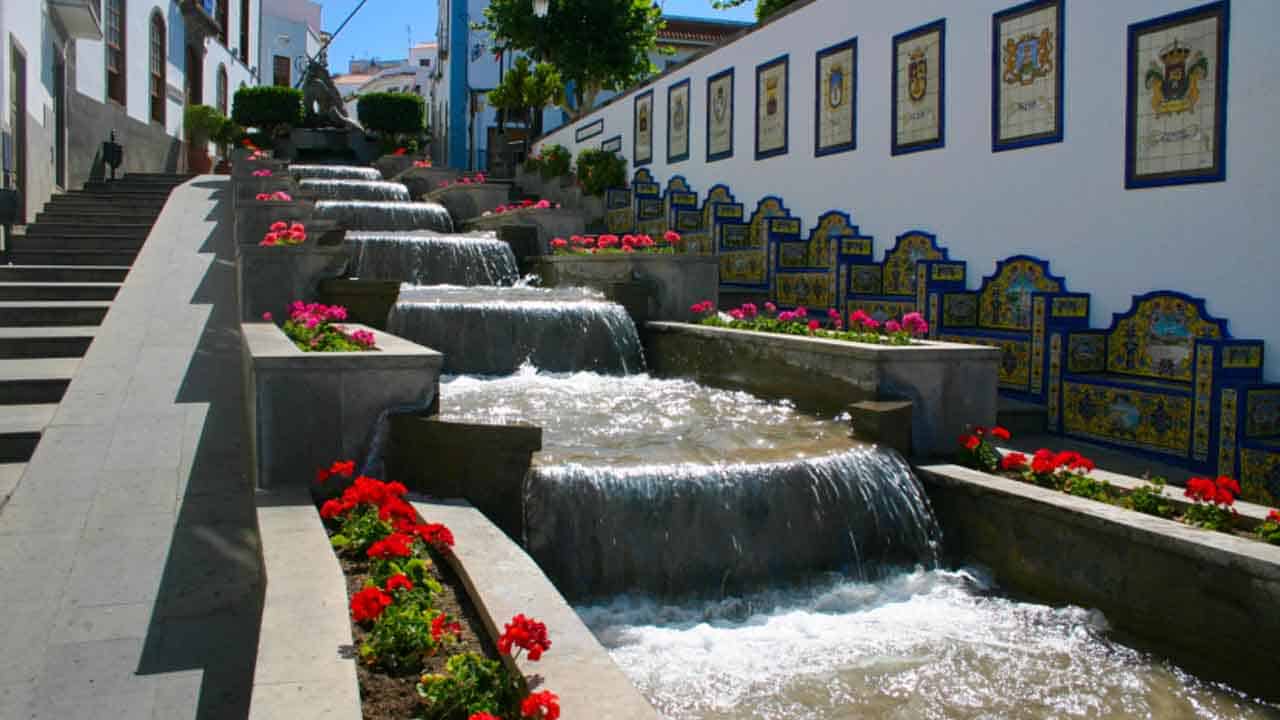 Water feature with cascading waterfalls and colourful flowers in a picturesque village setting.