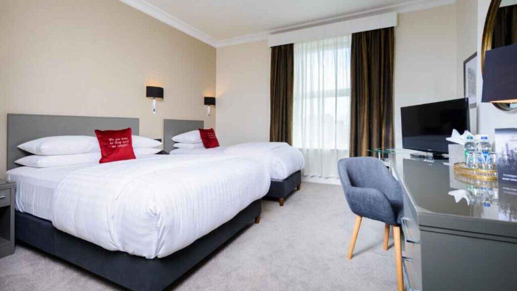 Comfortable hotel room with twin beds, modern decor, and a workspace with a TV and water bottles for.