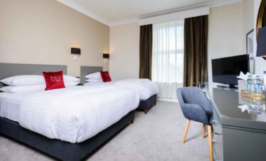 Comfortable hotel room with twin beds, modern decor, and a workspace with a TV and water bottles for.