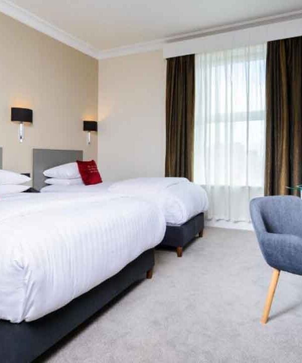 Comfortable hotel room with twin beds, modern decor, and a workspace with a TV and water bottles for.