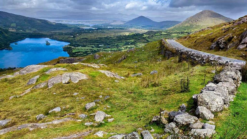 Beautiful Irish landscape featuring a lake, rolling hills, and distant mountains under a partly clou.