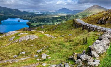 Beautiful Irish landscape featuring a lake, rolling hills, and distant mountains under a partly clou.