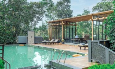 Outdoor pool with a stylish glass pavilion surrounded by trees and nature.