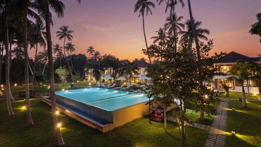 Beautiful tropical resort pool surrounded by palm trees at sunset.