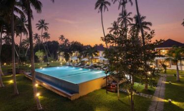 Beautiful tropical resort pool surrounded by palm trees at sunset.