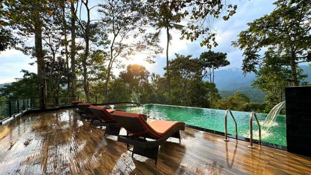 Infinity pool with lounge chairs in lush jungle setting at sunset.