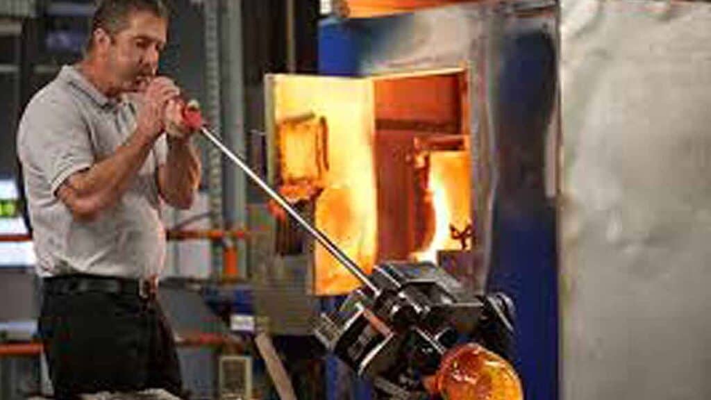 Glassblowing artist shaping molten glass with a blowpipe in a studio.