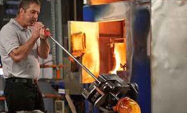 Glassblowing artist shaping molten glass with a blowpipe in a studio.