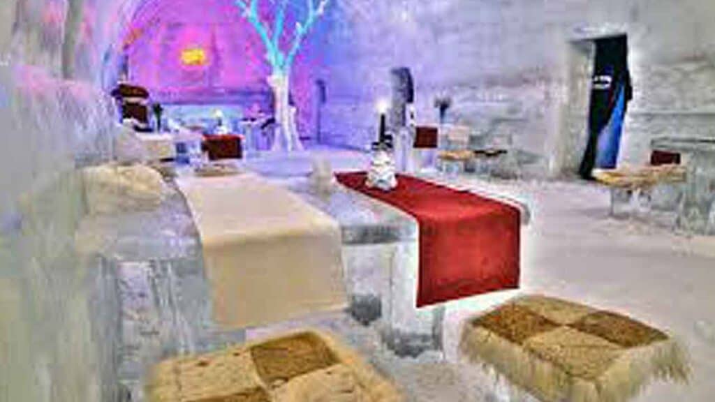 Ice hotel lounge with colourful lighting and ice furniture for a unique holiday experience.