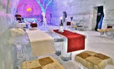 Ice hotel lounge with colourful lighting and ice furniture for a unique holiday experience.
