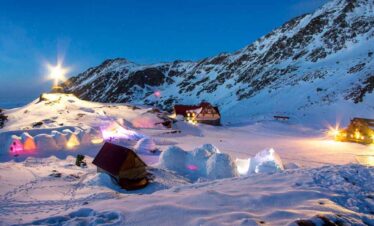 Snow-covered mountain landscape with tents and cabins at dusk.