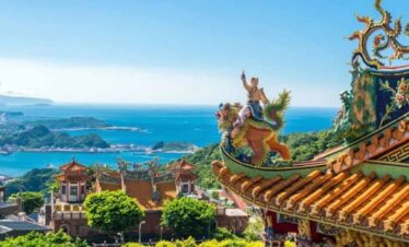 Asian temple with dragon sculpture overlooking scenic coastal landscape.