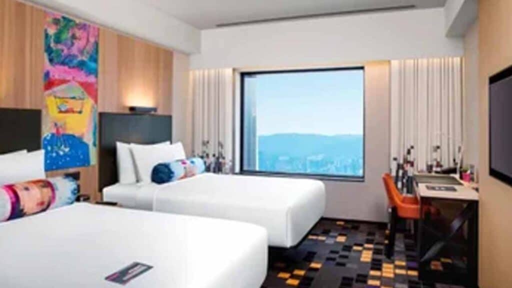Modern hotel room with two beds and a large window overlooking scenic mountains.