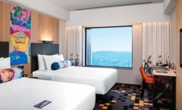 Modern hotel room with two beds and a large window overlooking scenic mountains.
