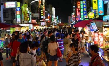 Night market bustling with shoppers and food stalls in Asia.