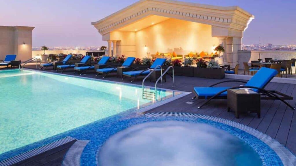 Rooftop pool with sun loungers and city view at sunset.
