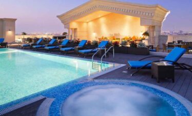 Rooftop pool with sun loungers and city view at sunset.