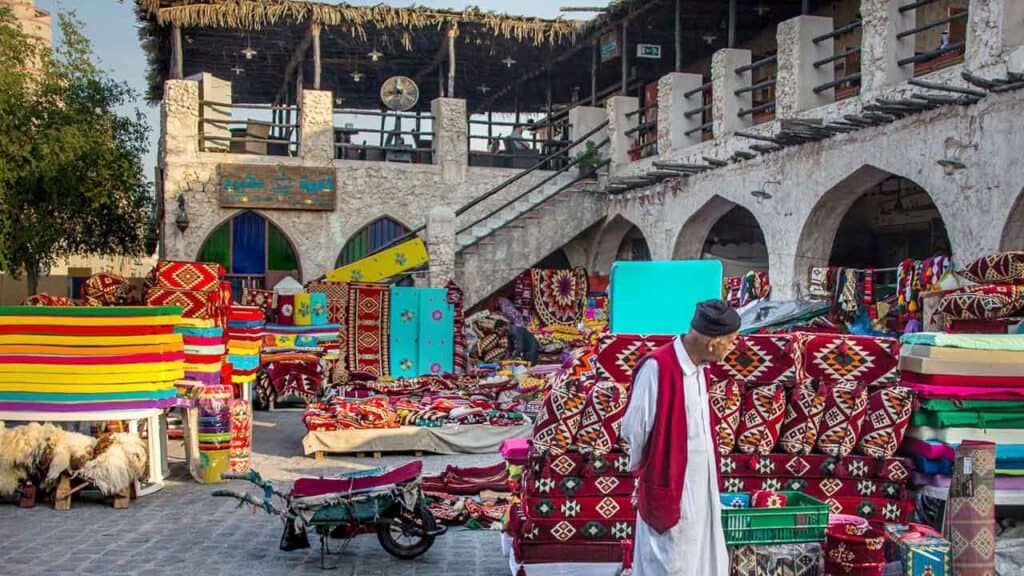Colourful market stall displaying rugs, textiles, and souvenirs in an outdoor setting.