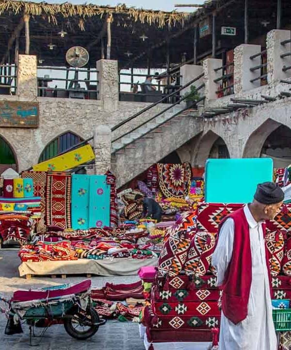 Colourful market stall displaying rugs, textiles, and souvenirs in an outdoor setting.