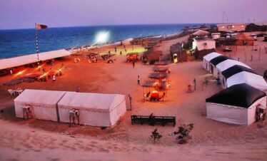 Beachside camping at sunset with tents and the ocean in the background.