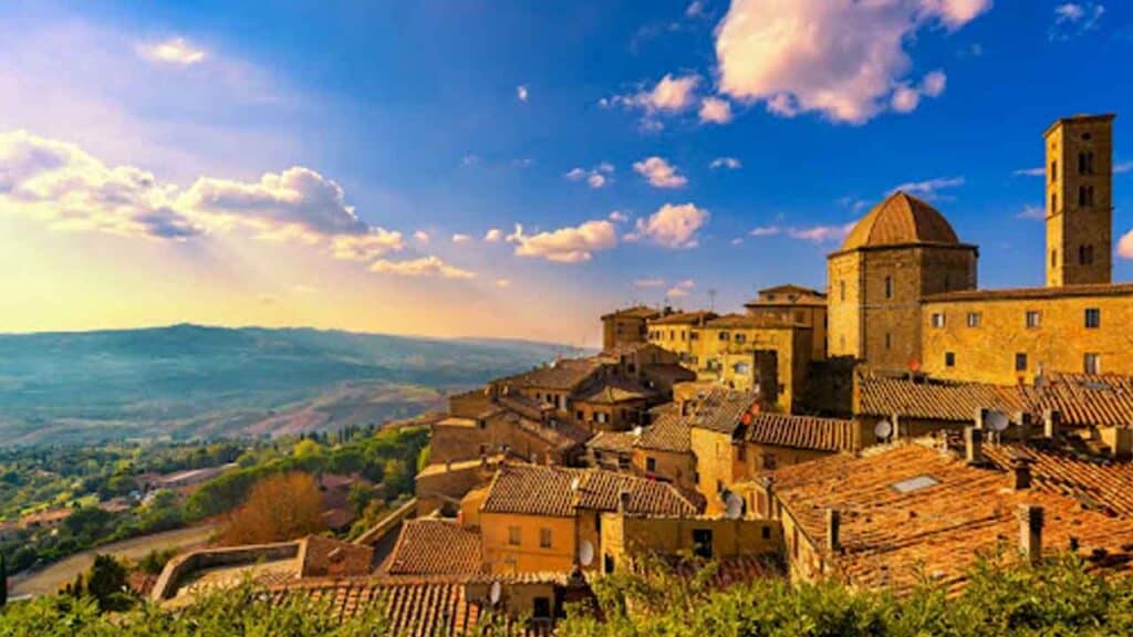Ancient Tuscan village with stone buildings and a castle, set against a scenic landscape at sunset.