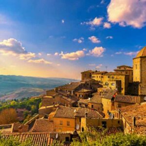 Ancient Tuscan village with stone buildings and a castle, set against a scenic landscape at sunset.