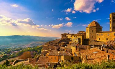 Ancient Tuscan village with stone buildings and a castle, set against a scenic landscape at sunset.