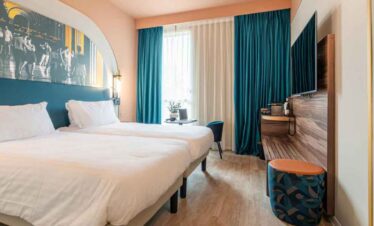 Bright hotel room with a large bed, vibrant curtains, and a flat-screen TV for a comfortable stay.