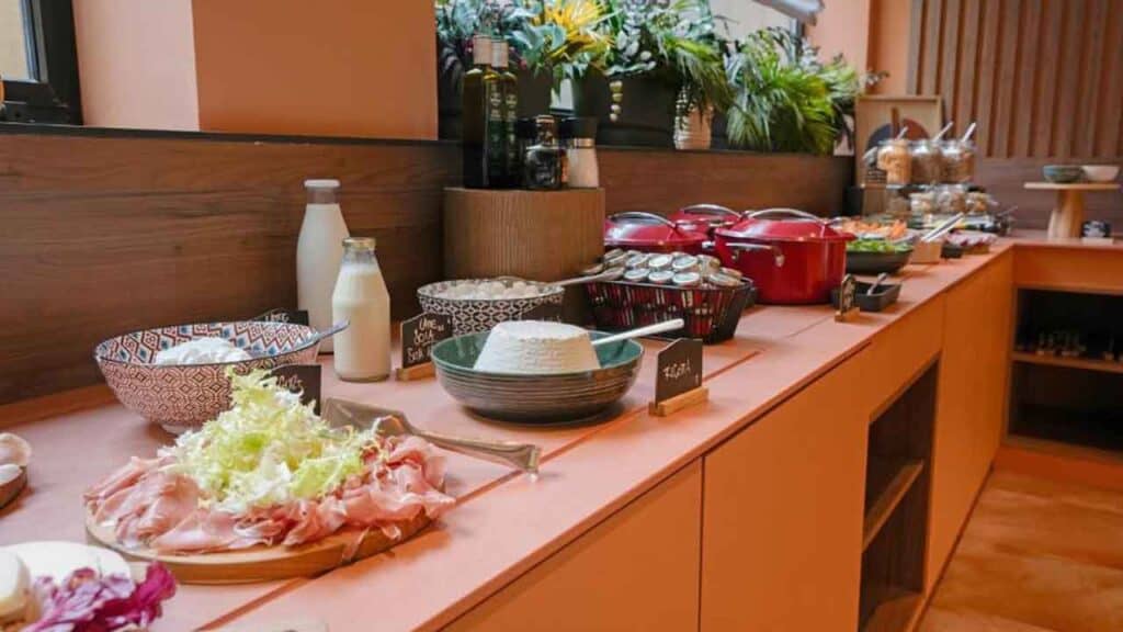 Buffet table with breakfast options including bread, drinks, and fresh ingredients.