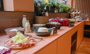 Buffet table with breakfast options including bread, drinks, and fresh ingredients.