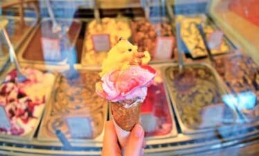 Ice cream cone with colourful scoops and toppings in a gelato shop.
