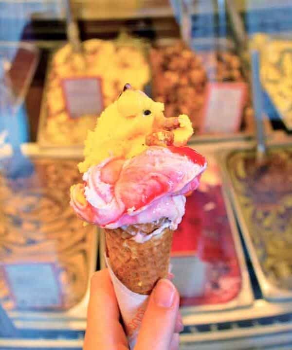 Ice cream cone with colourful scoops and toppings in a gelato shop.