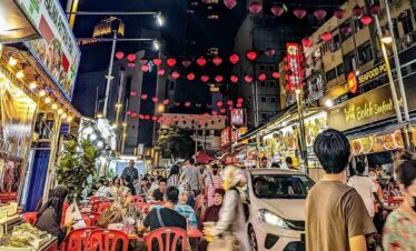 Vibrant night market with food stalls, lanterns, and busy crowds in an Asian city.