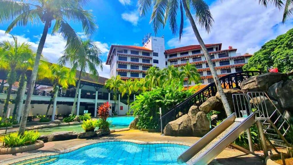 Beautiful tropical resort featuring a swimming pool surrounded by lush palm trees and vibrant greene.