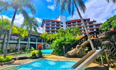 Beautiful tropical resort featuring a swimming pool surrounded by lush palm trees and vibrant greene.