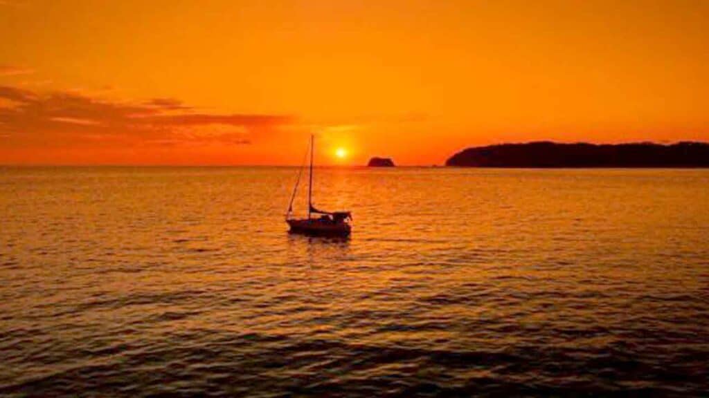 Sunset over tranquil sea with a sailboat during golden hour.