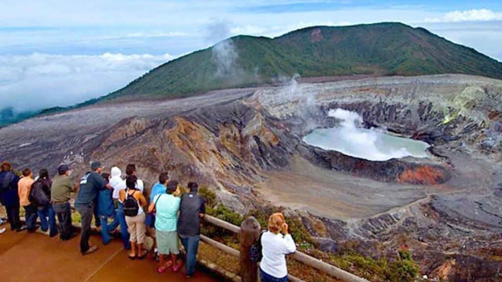 Tourists observing erupting volcano crater in a scenic landscape.