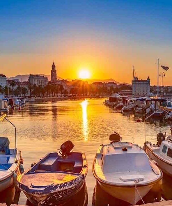 Harbour at sunset with boats, palm trees, and calm waters.
