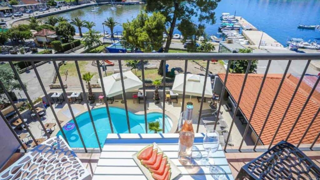 Balcony overlooking a marina with a pool, outdoor dining, and lush greenery in a scenic holiday dest.