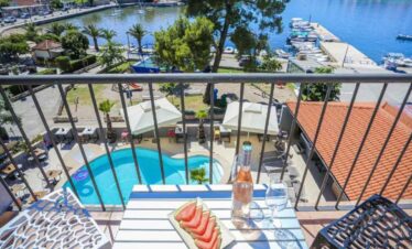 Balcony overlooking a marina with a pool, outdoor dining, and lush greenery in a scenic holiday dest.