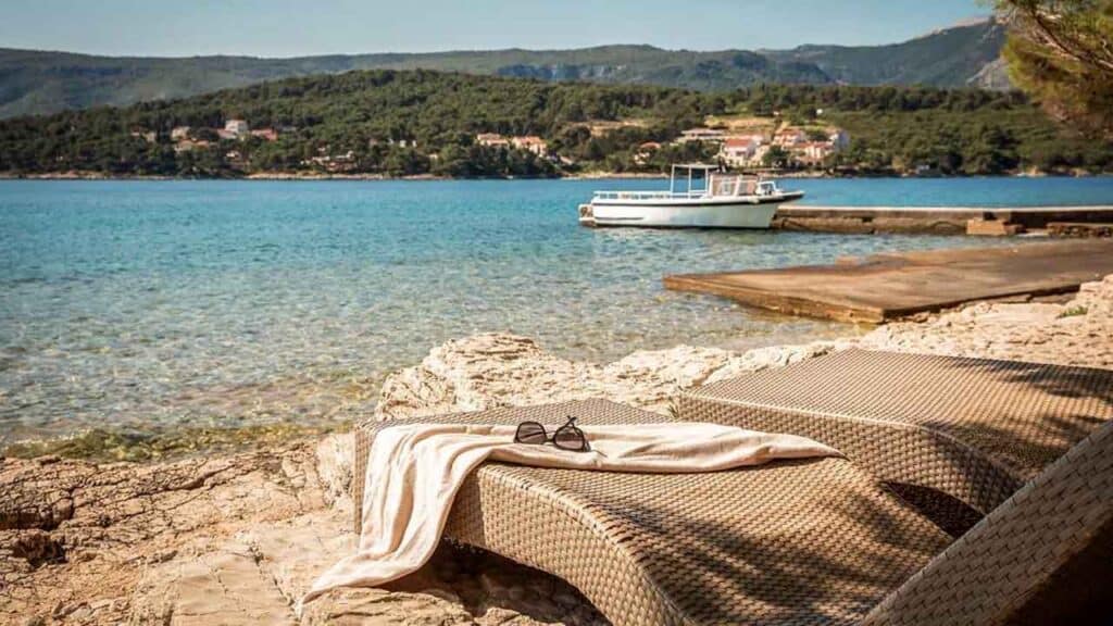 Relaxing lakeside scene with sun loungers and boat in the background.